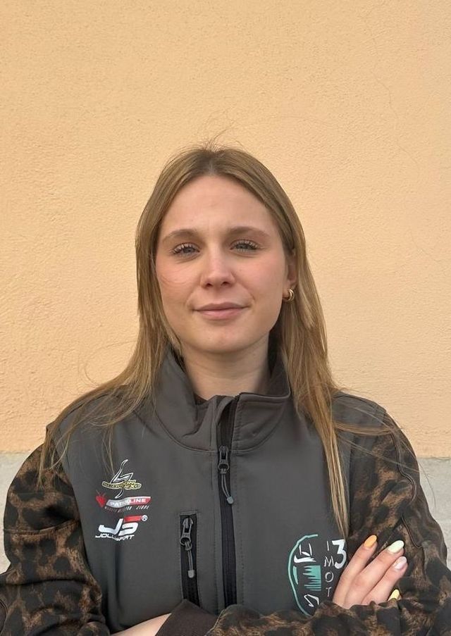 Una persona con lunghi capelli biondi, che indossa un gilet grigio sopra una giacca leopardata, è in