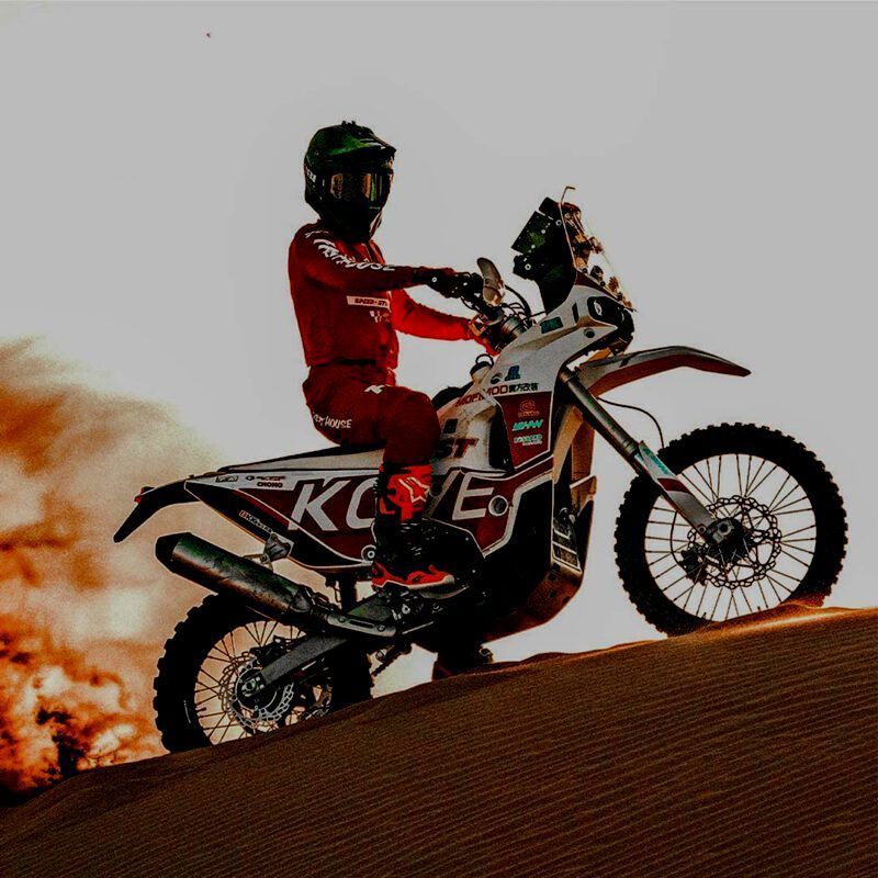 Un motociclista vestito di rosso è seduto su una moto da rally Kove in cima a una duna di sabbia,