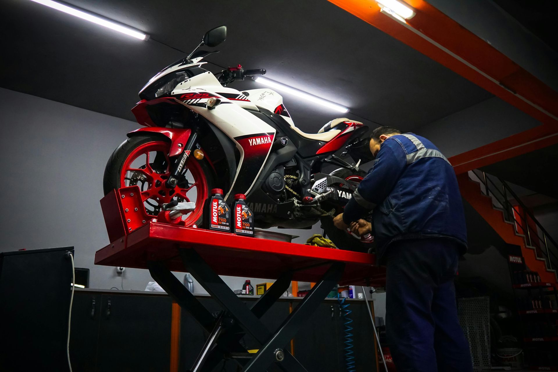 In un'officina, un meccanico in tuta da lavoro blu scuro effettua la manutenzione di una motocicletta sportiva