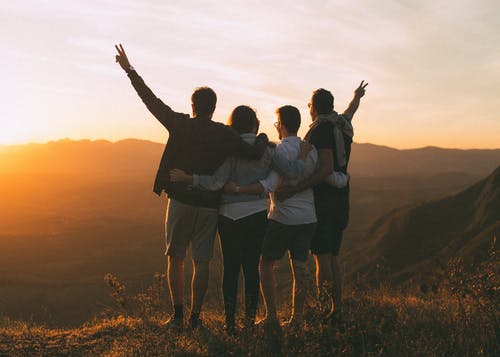 Four friends arms around each other at sunset