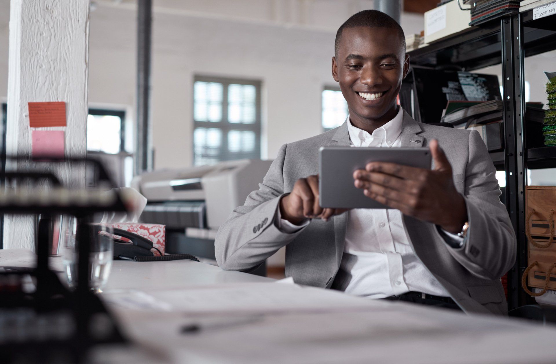 A man in a suit is sitting at a desk using a tablet computer.