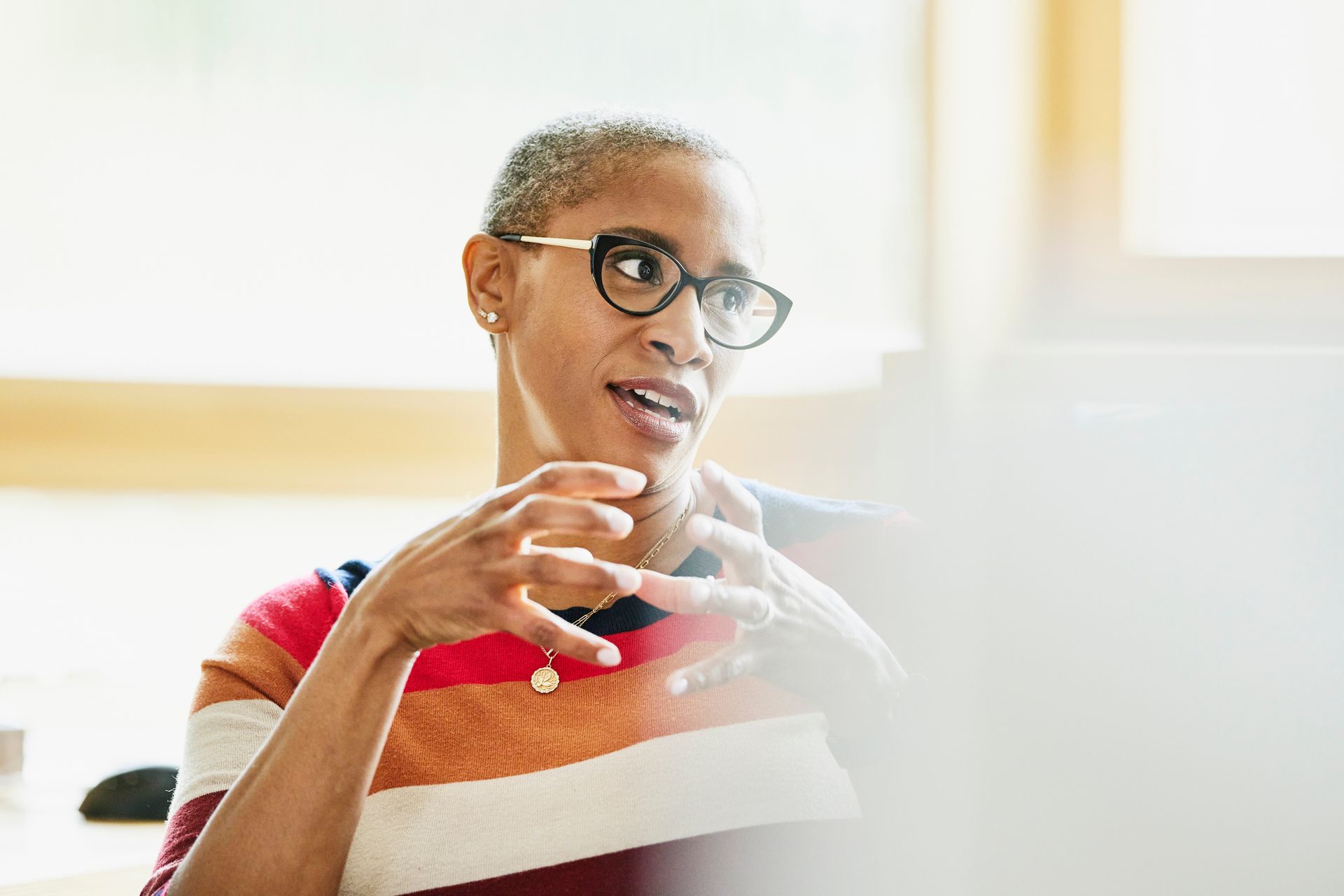 A woman wearing glasses is sitting at a table talking to someone.