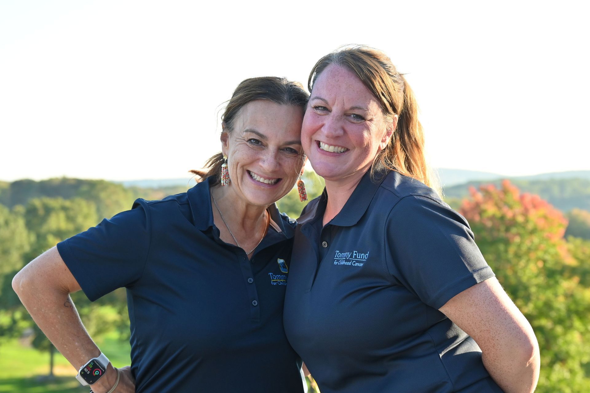 Two women wearing helmets and shirts that say team tommy fund