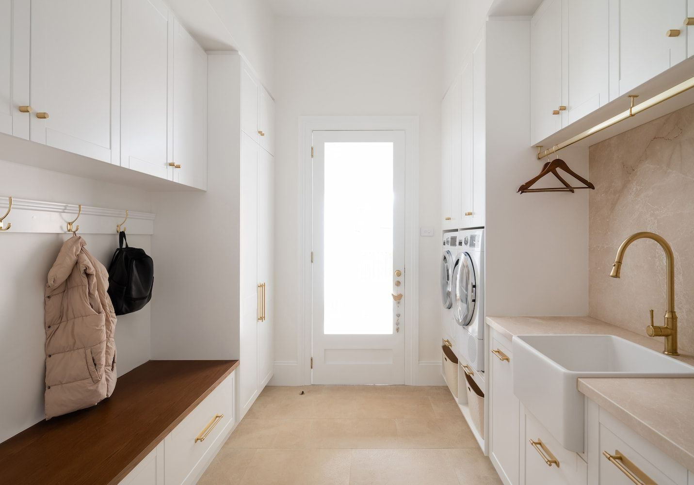 Laundry Room With White Cabinets, Wood Bench, Gold Hardware, and a Doorway — Garry Jeans Kitchens In Cardiff, NSW