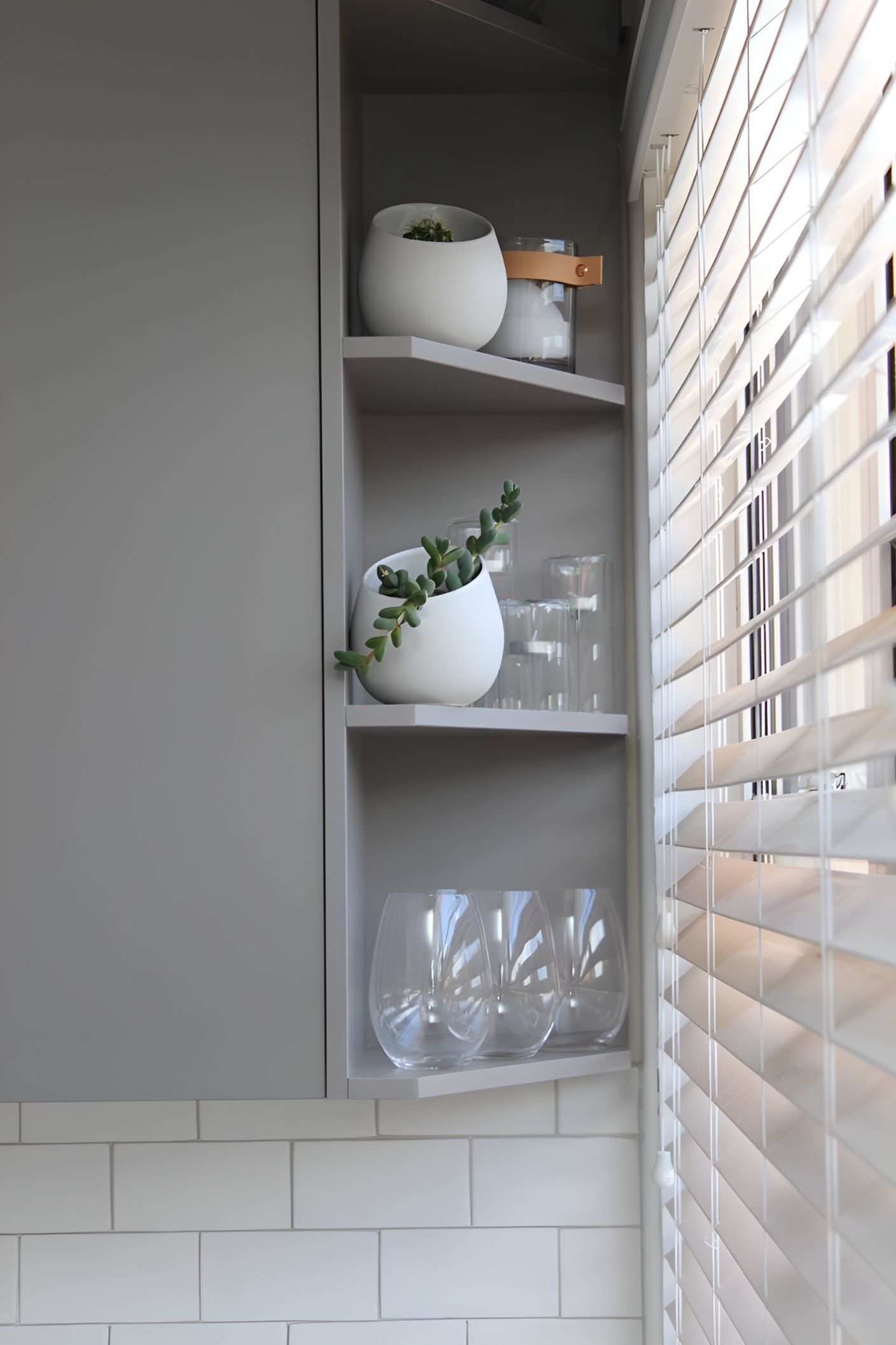 A Kitchen With a Shelf Filled With Glasses and Potted Plants Next to a Window — Garry Jeans Kitchens In Cardiff, NSW