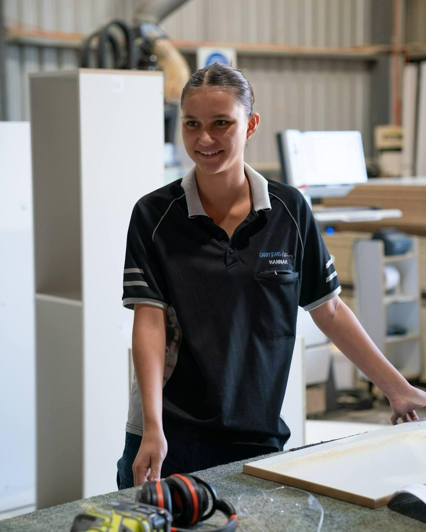 A Woman In A Black Shirt Is Standing Next To A Table In A Workshop — Garry Jeans Kitchens In Newcastle, NSW