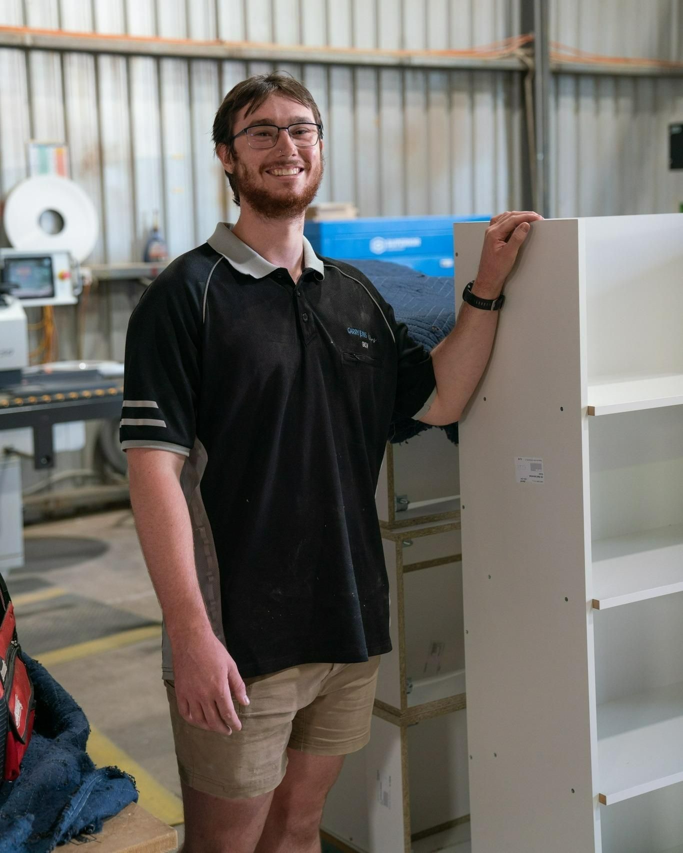 A Man Is Leaning Against A White Shelf In A Warehouse — Garry Jeans Kitchens In Maitland, NSW