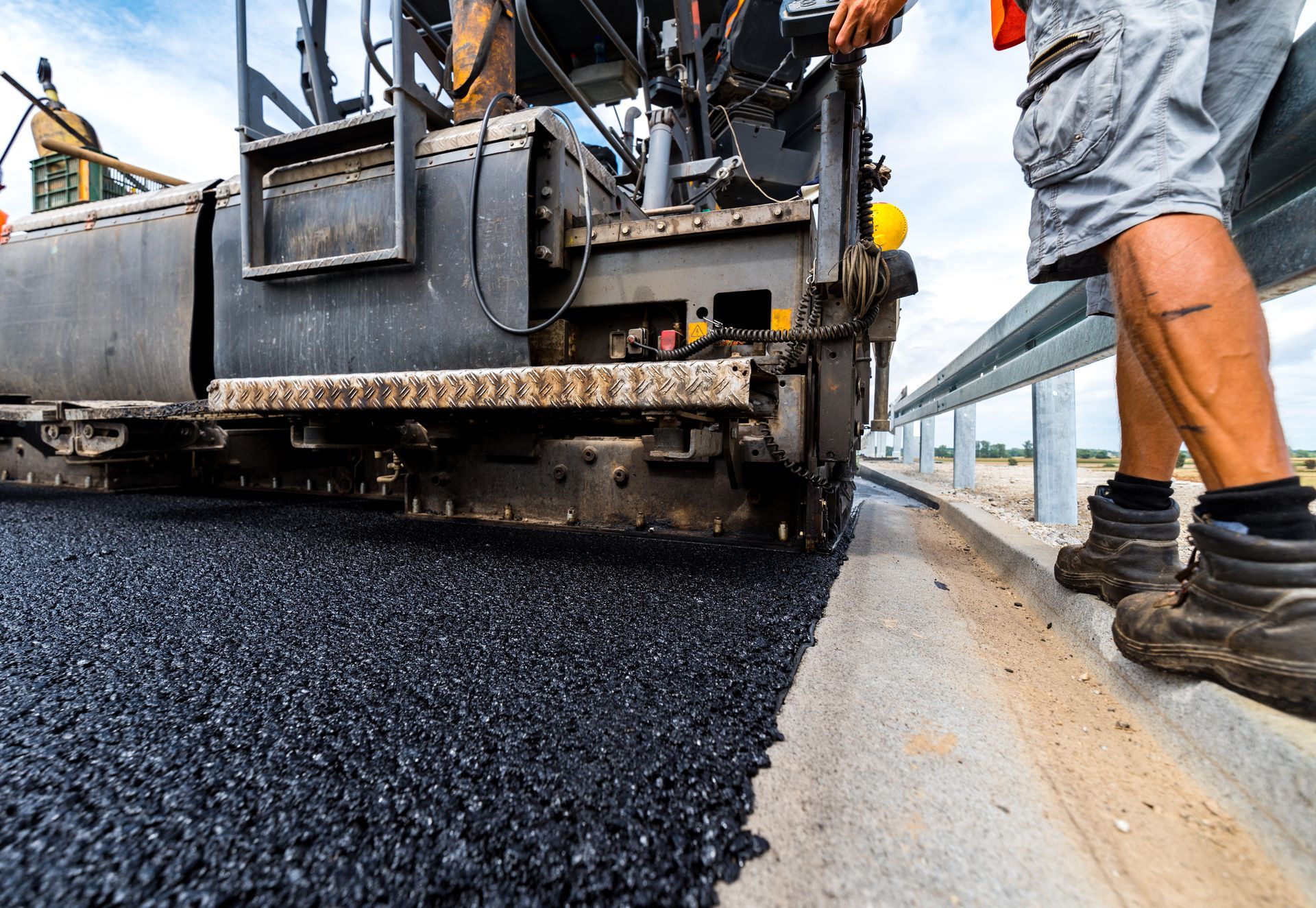 Construction crew using asphalt paving machine to lay fresh blacktop on urban road during daylight.