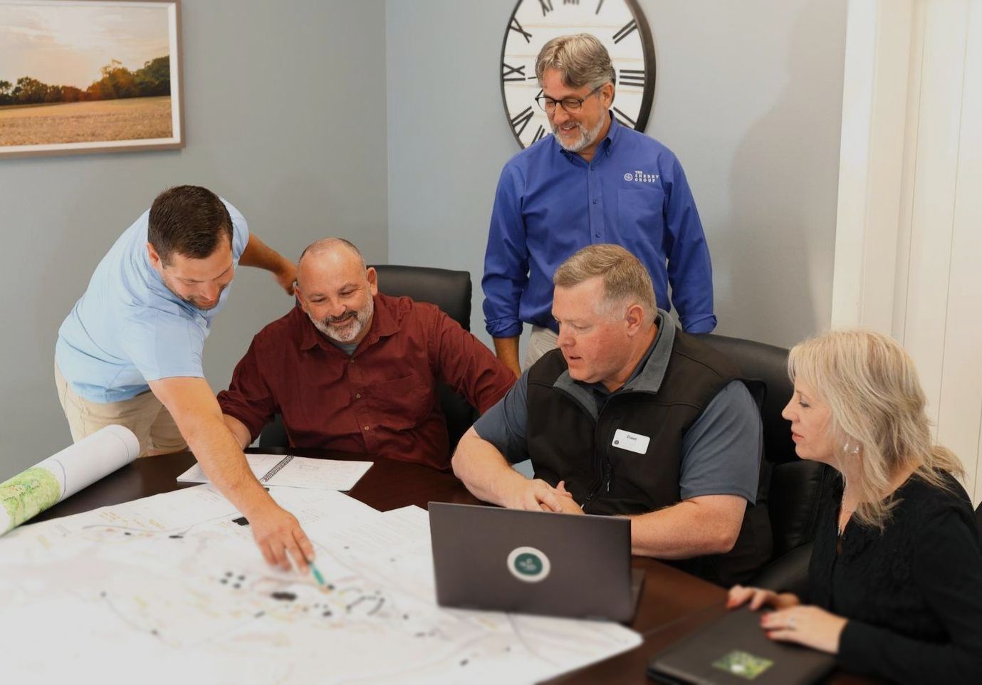The Sherry Group Logo A group of people are sitting around a table looking at a laptop.