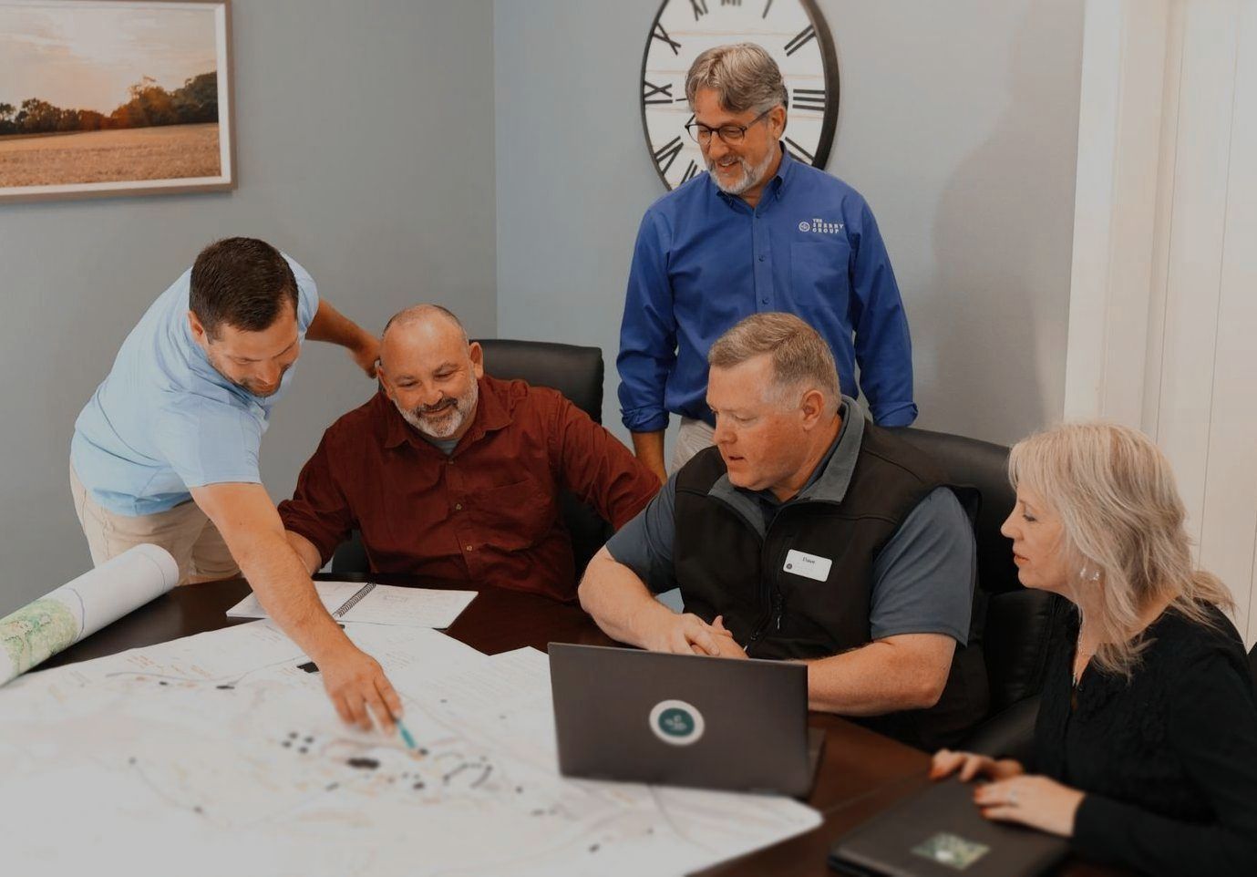 A group of people are sitting around a table looking at a laptop.