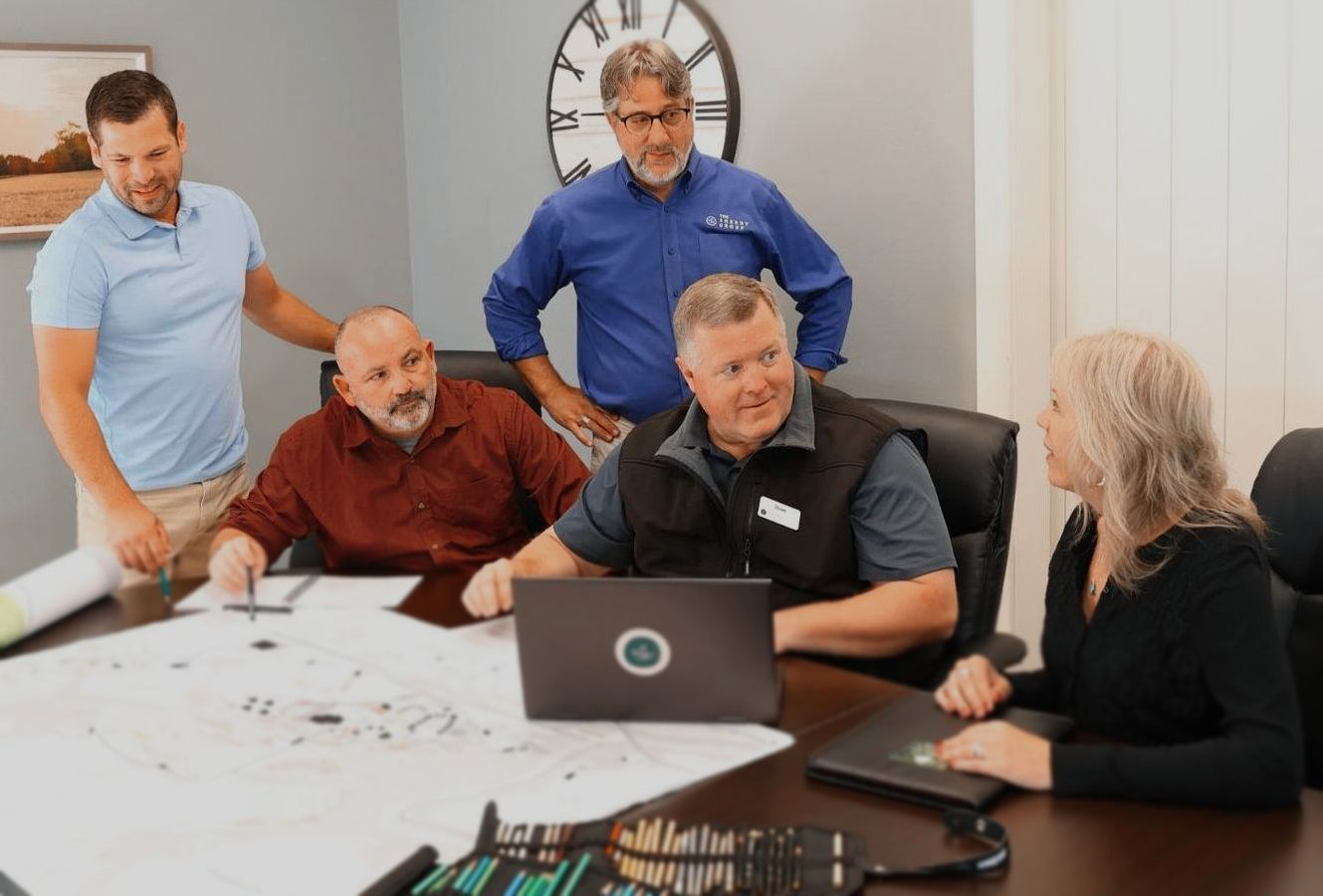 A group of people are sitting around a table looking at a laptop.