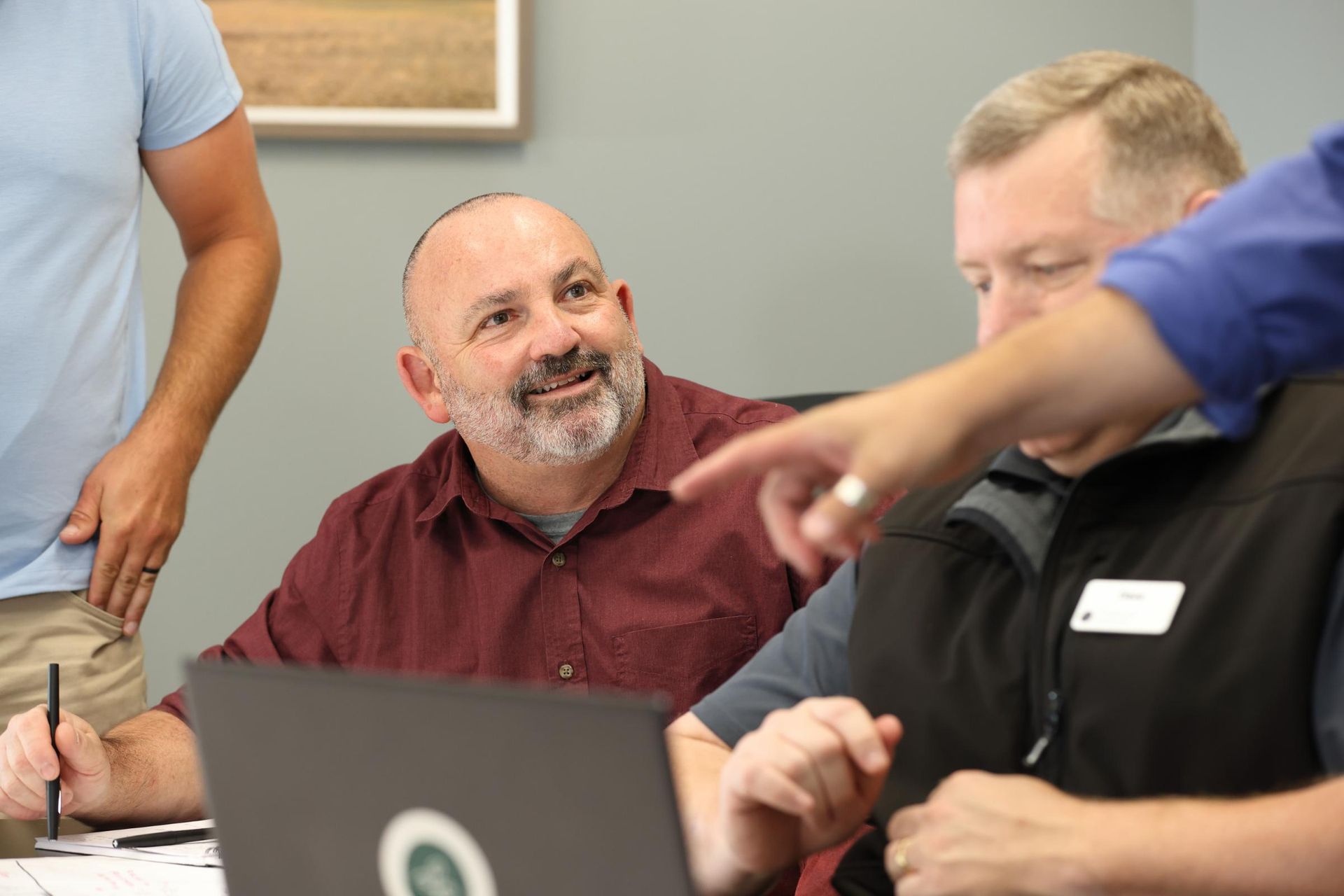 A group of men are sitting around a table looking at a laptop computer.
