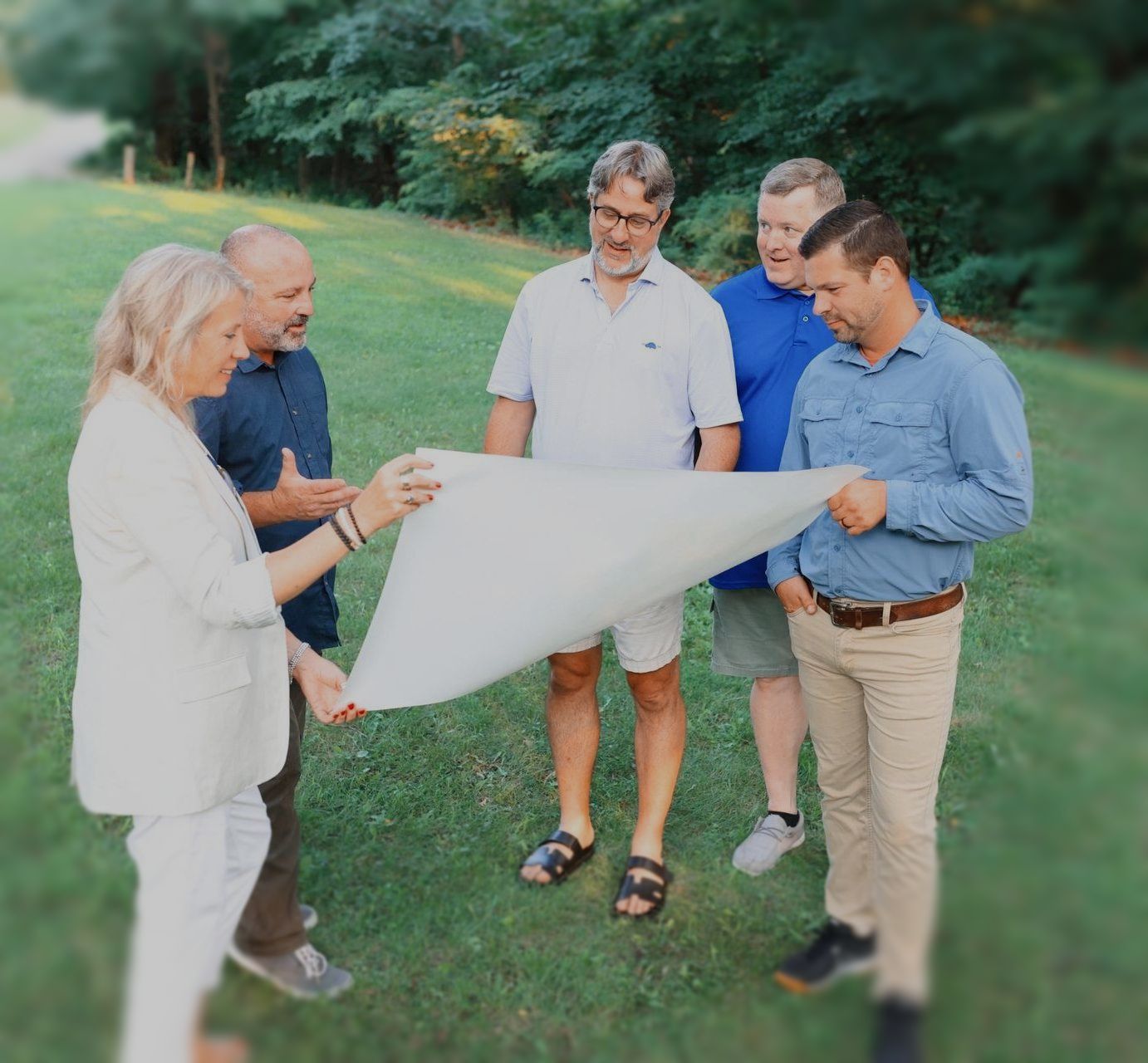 A group of people are standing in the grass looking at a piece of paper