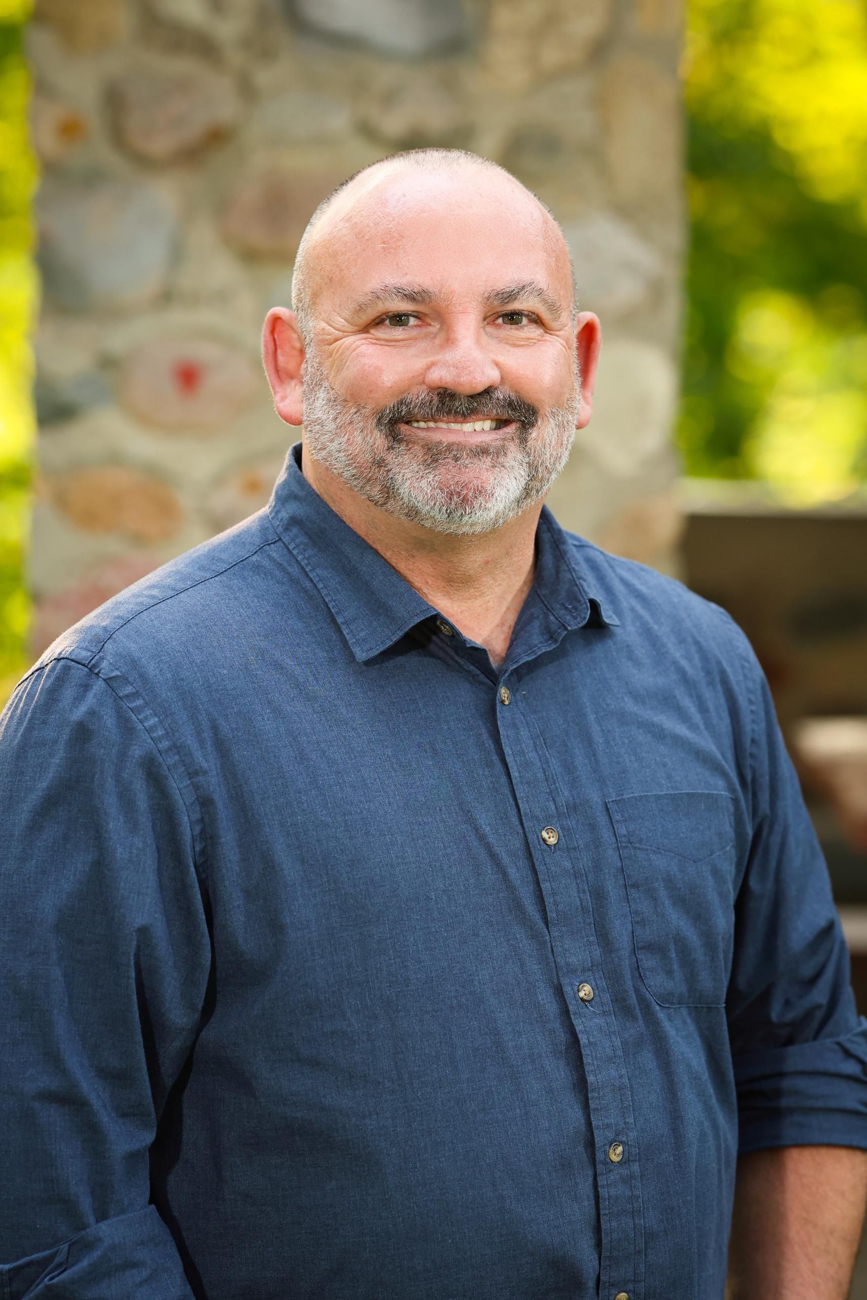 A man with a beard and mustache is wearing a blue shirt and smiling.