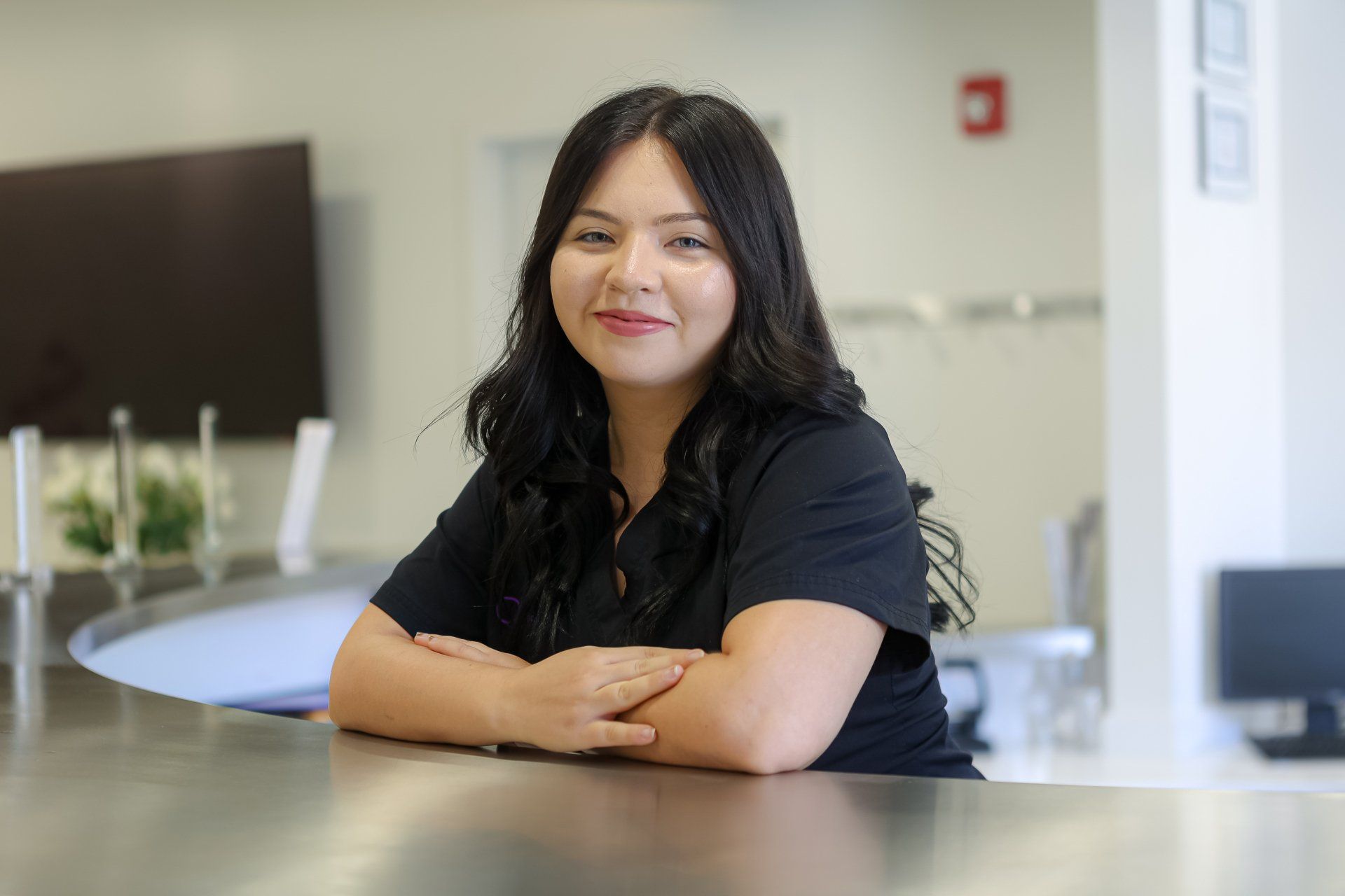 A woman is sitting at a counter with her arms crossed and smiling.
