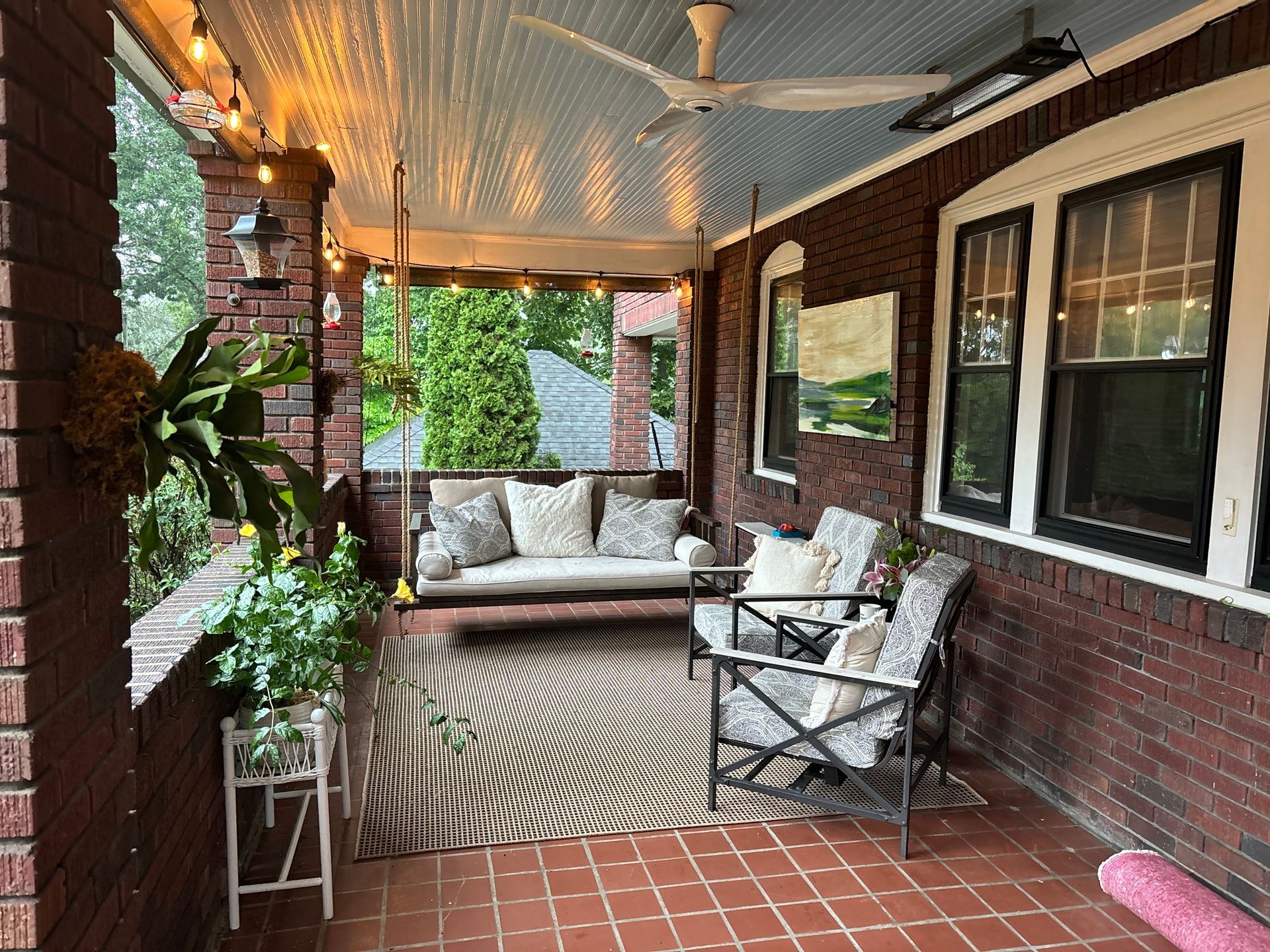 A porch with a swing , couch , chairs and a ceiling fan.