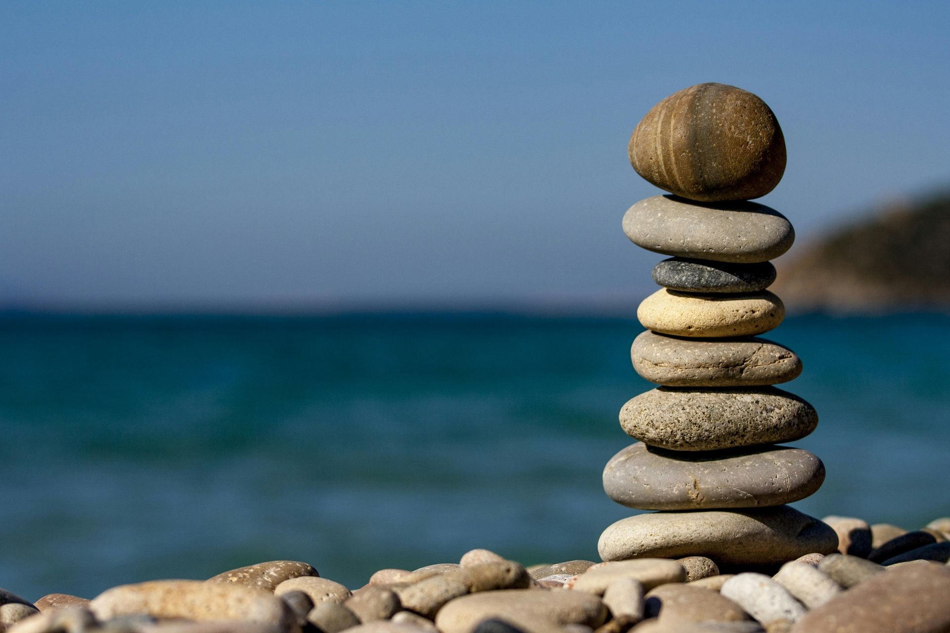 Stack of balanced stones on a pebbled beach, with ocean and blue sky in the background.