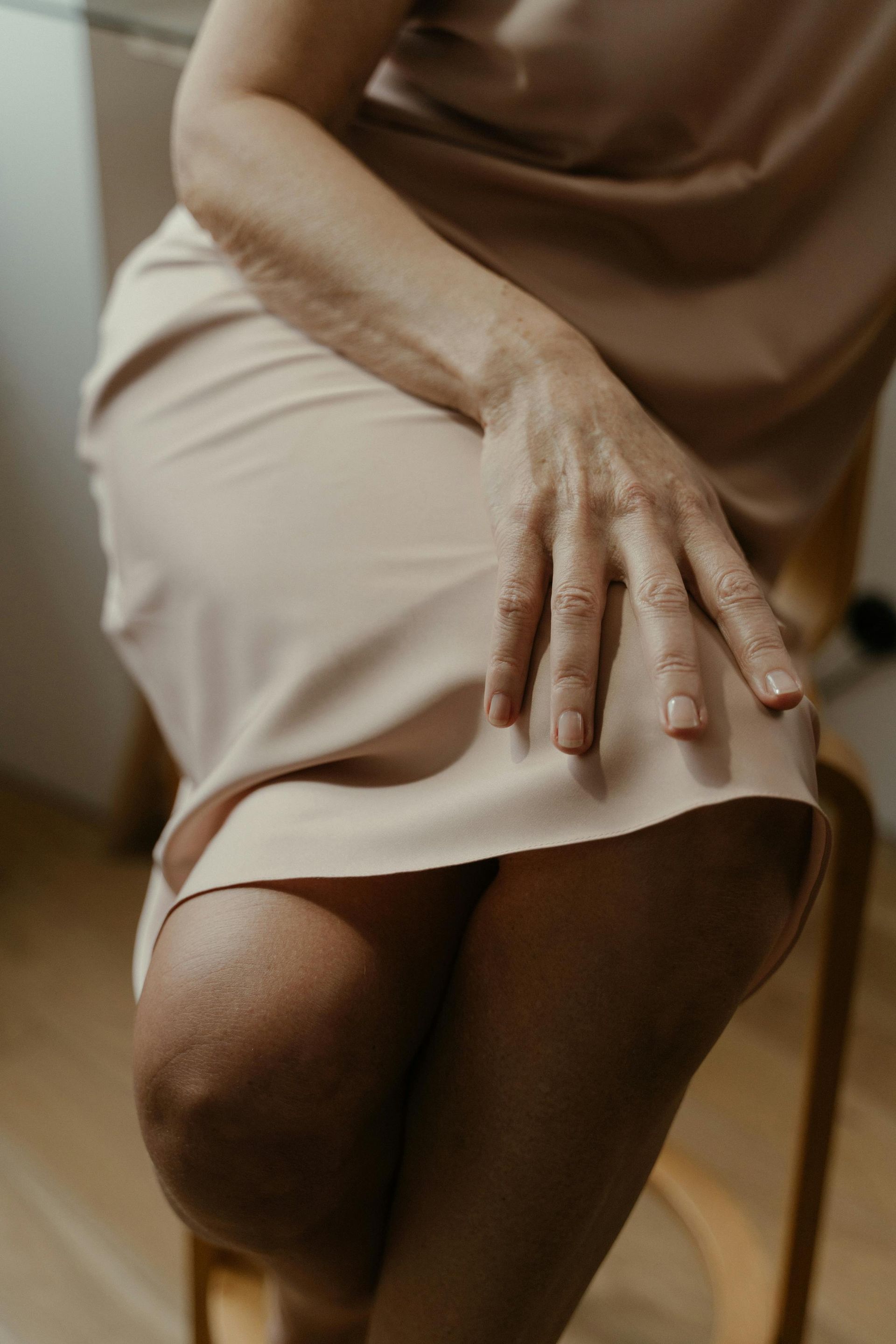A woman in a dress is sitting on a chair with her hands on her skirt.