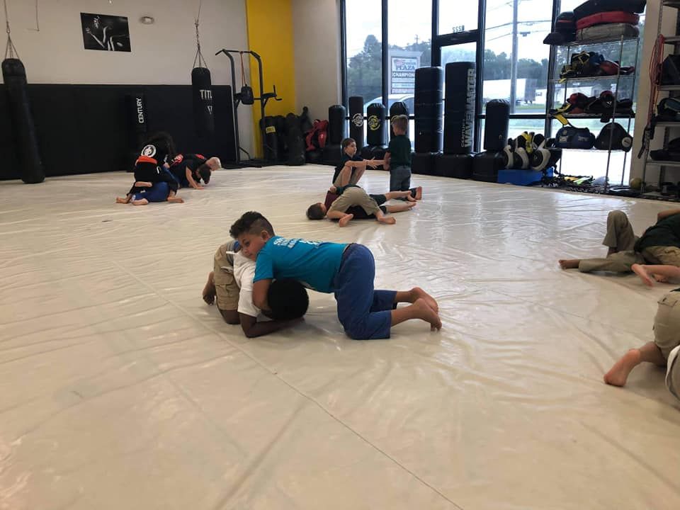 A group of children are wrestling on a mat in a gym.