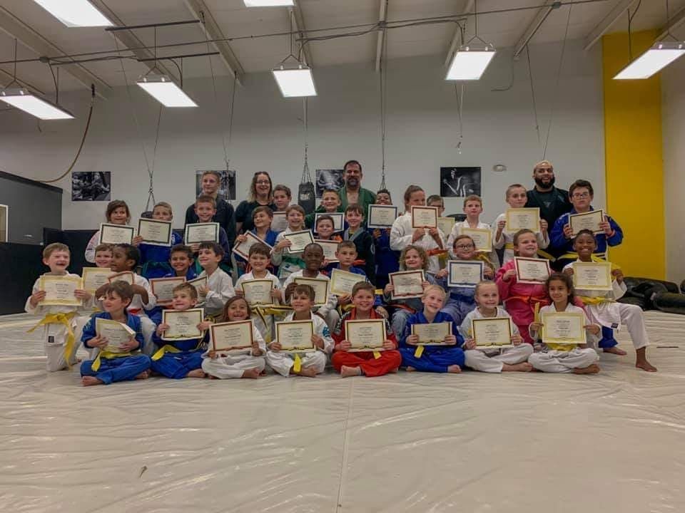 A group of children are posing for a picture in a gym holding certificates.