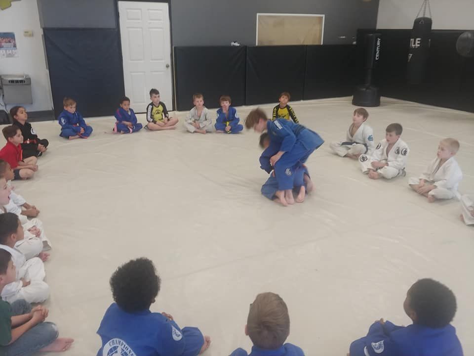 A group of children are sitting in a circle on the floor watching a karate class.