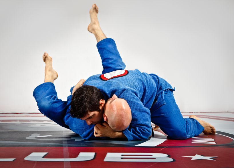 Two men in blue kimonos are wrestling on a wrestling mat.
