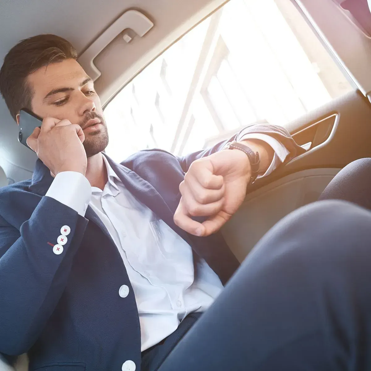 A man in a suit is talking on a cell phone and looking at his watch