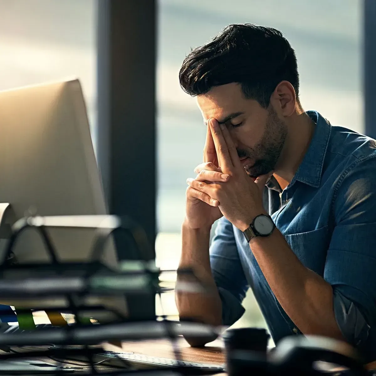 A man is sitting at a desk with his head in his hands in front of a computer.