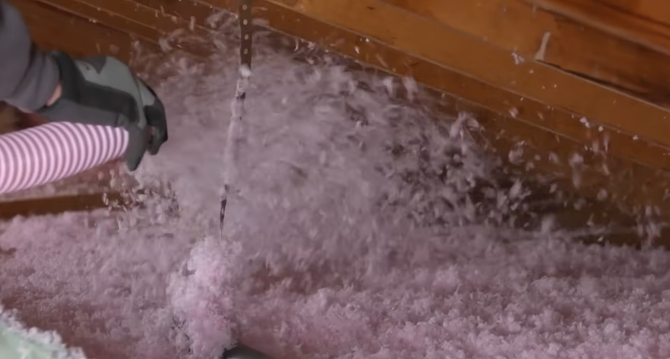 Worker in helmet spraying white insulation onto attic rafters