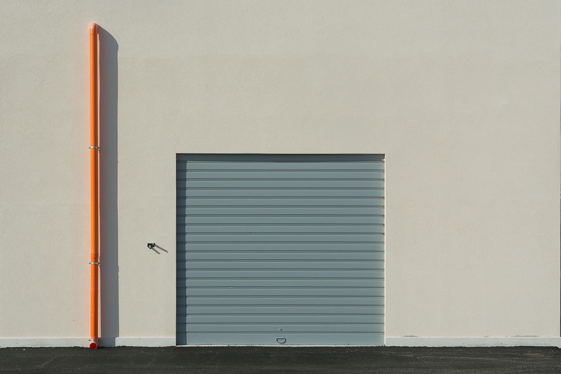 A building with a gray garage door and an orange pipe