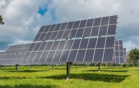 Solar panels in a grassy field under a cloudy sky.