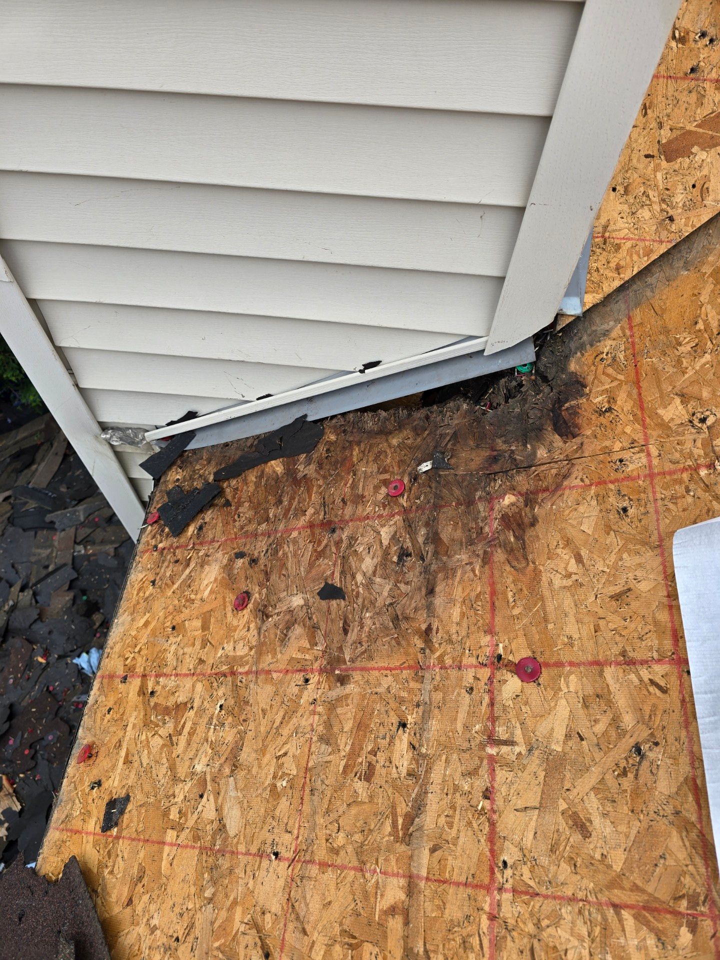 A section of a roof with rotted OSB sheathing and damaged shingles where a wall meets the roofline.