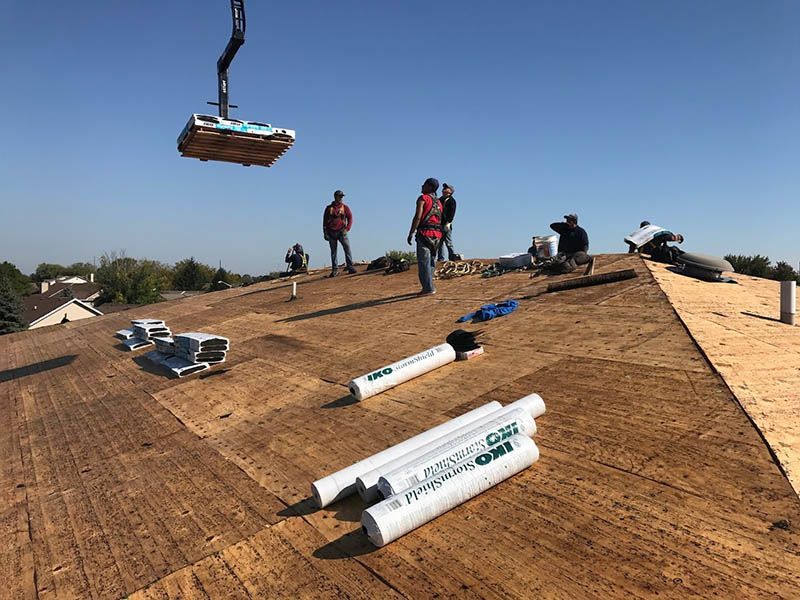 A crane is lifting a piece of plywood on top of a roof.