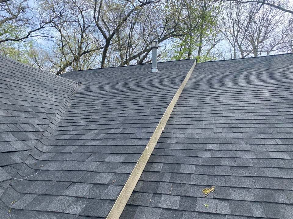 A roof with a wooden stick sticking out of it and trees in the background.
