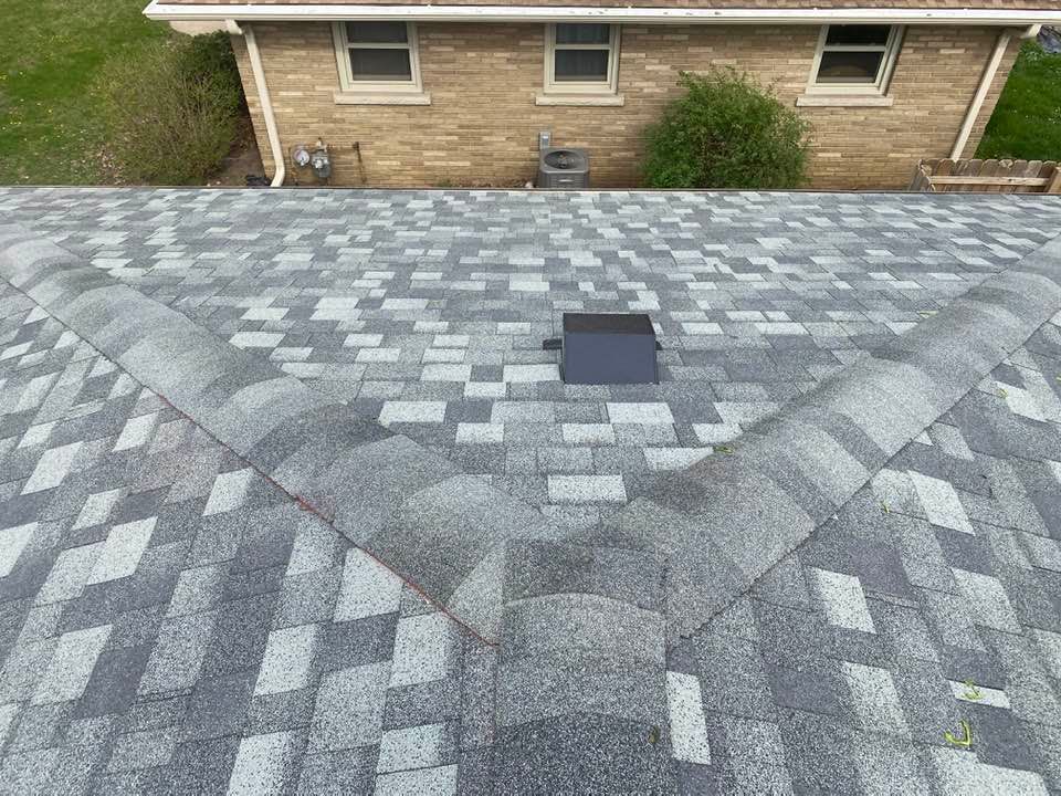 A roof with a hole in it and a brick house in the background.
