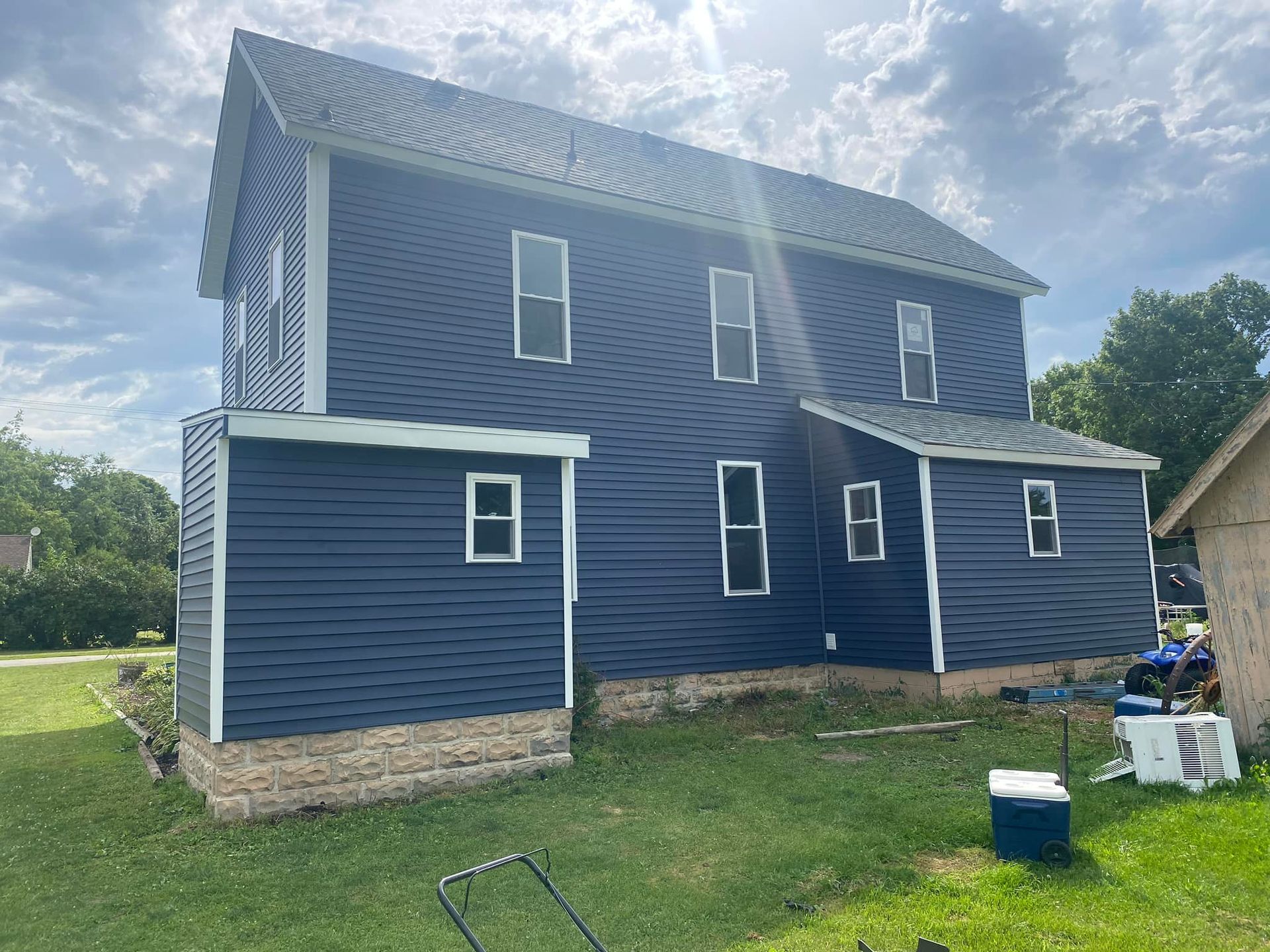 A blue house with white trim is sitting on top of a lush green field.