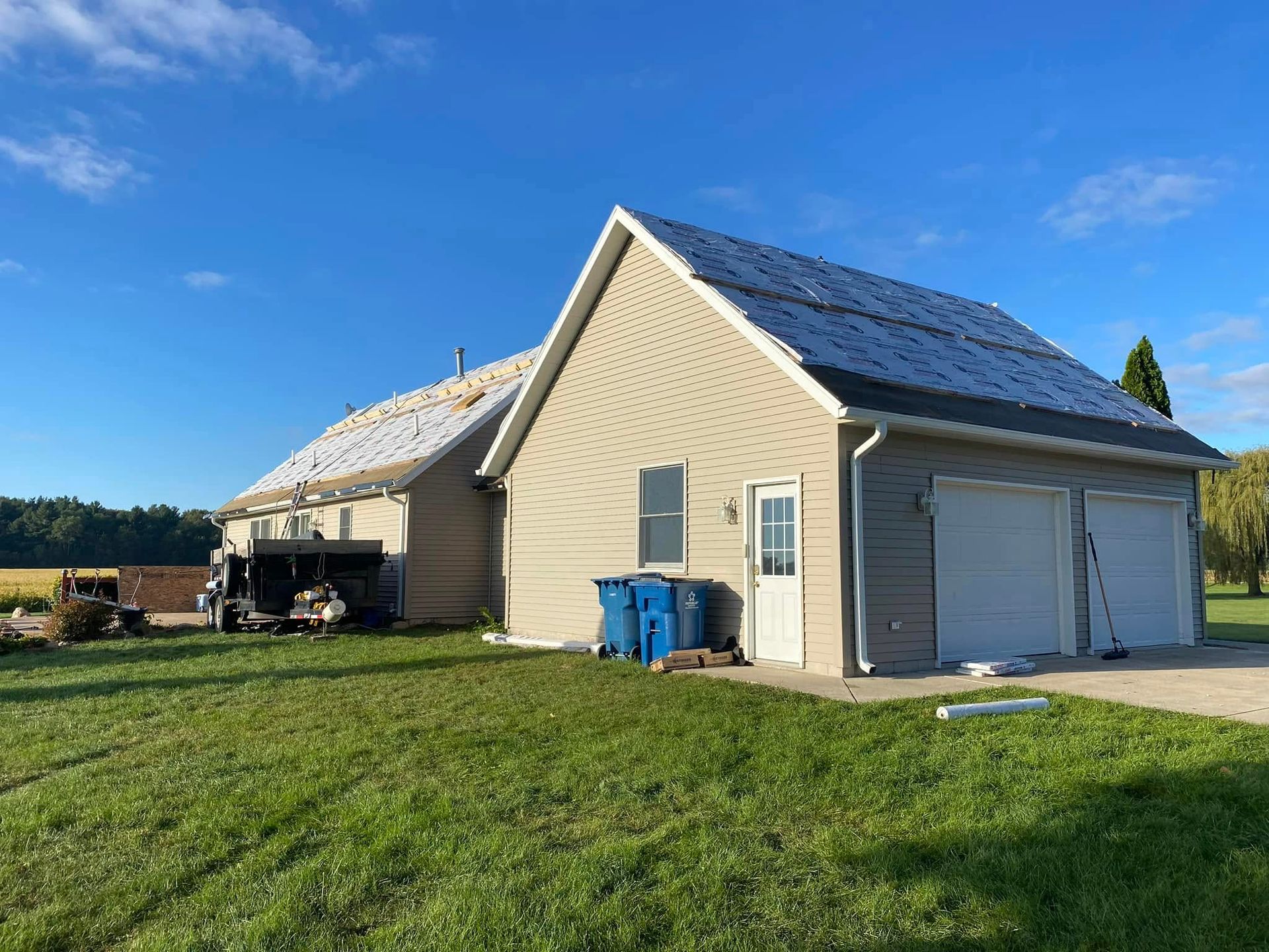 A house with a garage and a blue trash can in front of it.