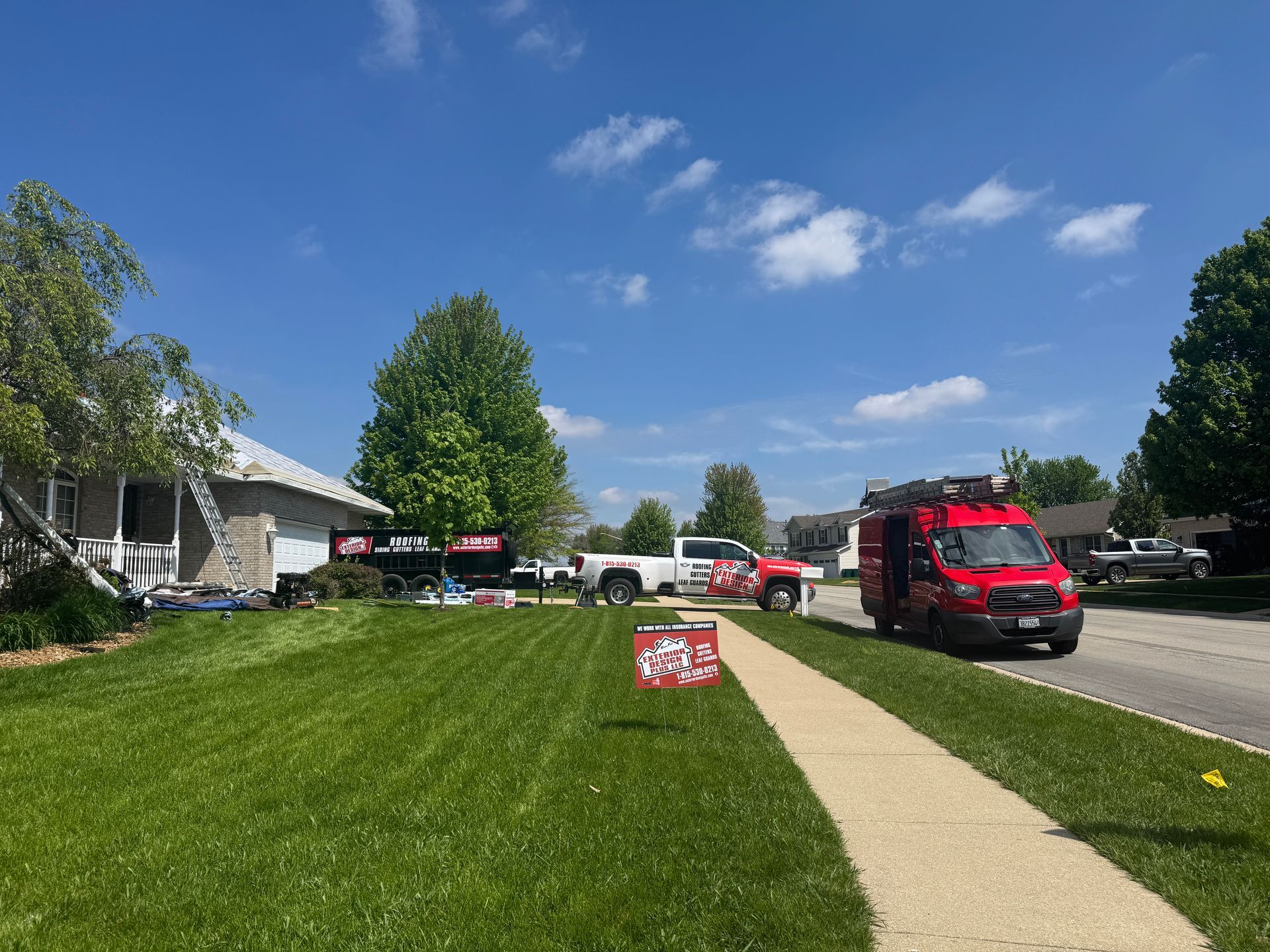 A red utility truck and a white pickup truck parked in front of a residential house on a sunny day with a green lawn.