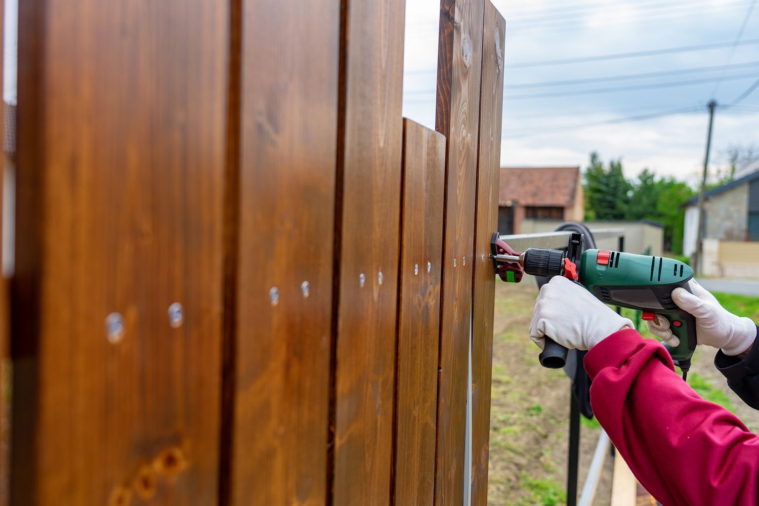Person using a green power drill to fasten a wooden fence post outdoors