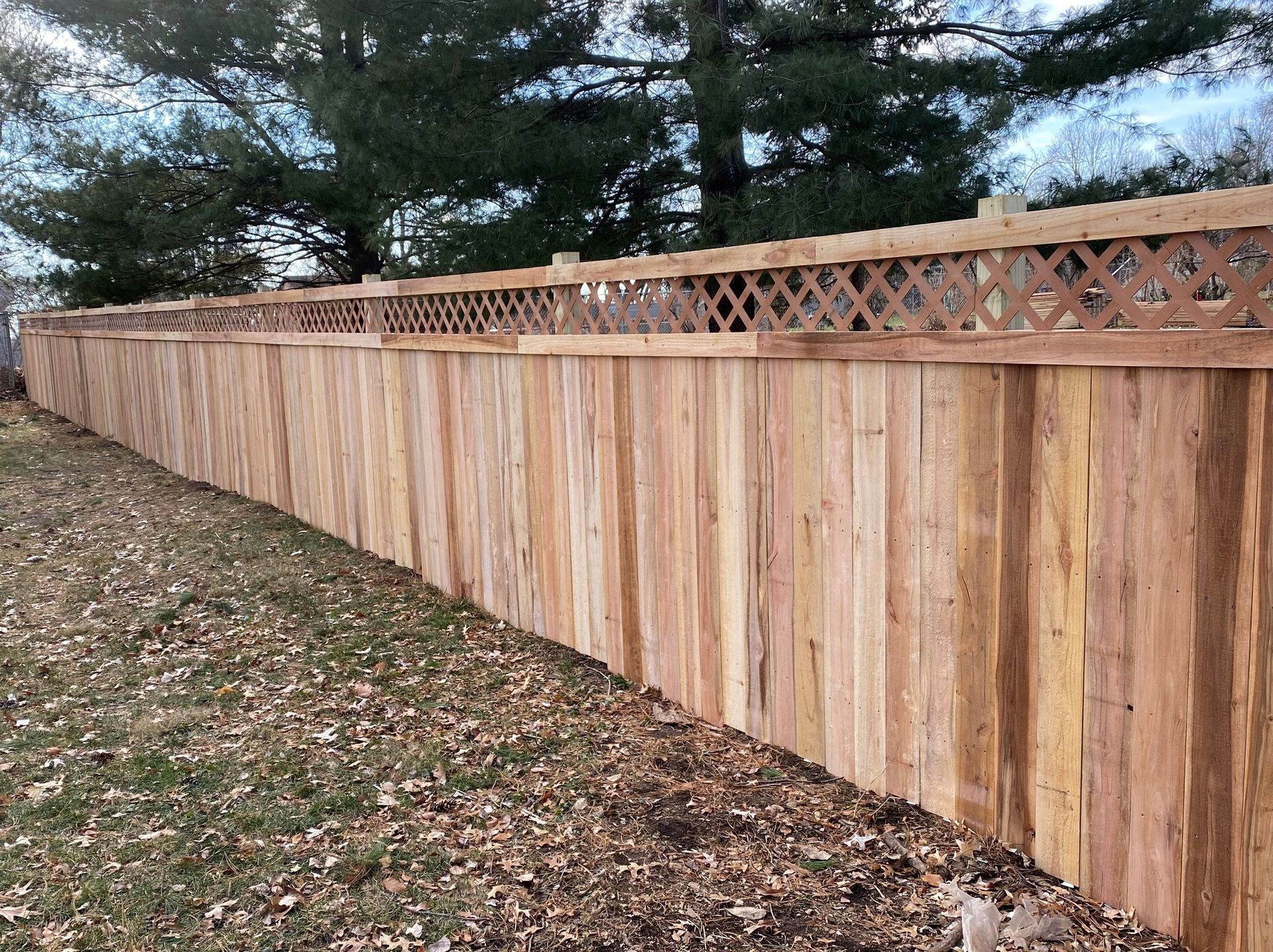 Long wooden privacy fence with a decorative lattice top along a leaf-covered yard