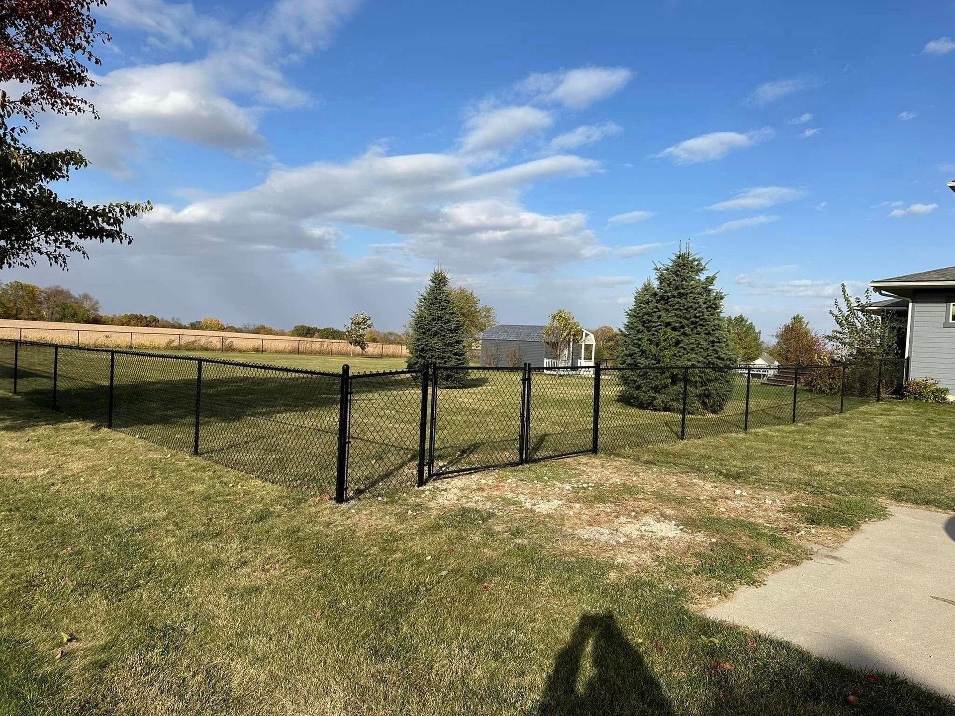 Grassy yard with black fence, trees, and a blue sky with scattered clouds
