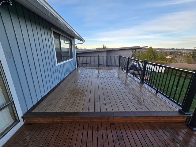 Wooden deck attached to a blue house, with black railing and a wide open view beyond.