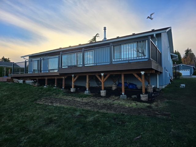 House on stilts with large windows at dusk, overlooking a grassy yard and lake.