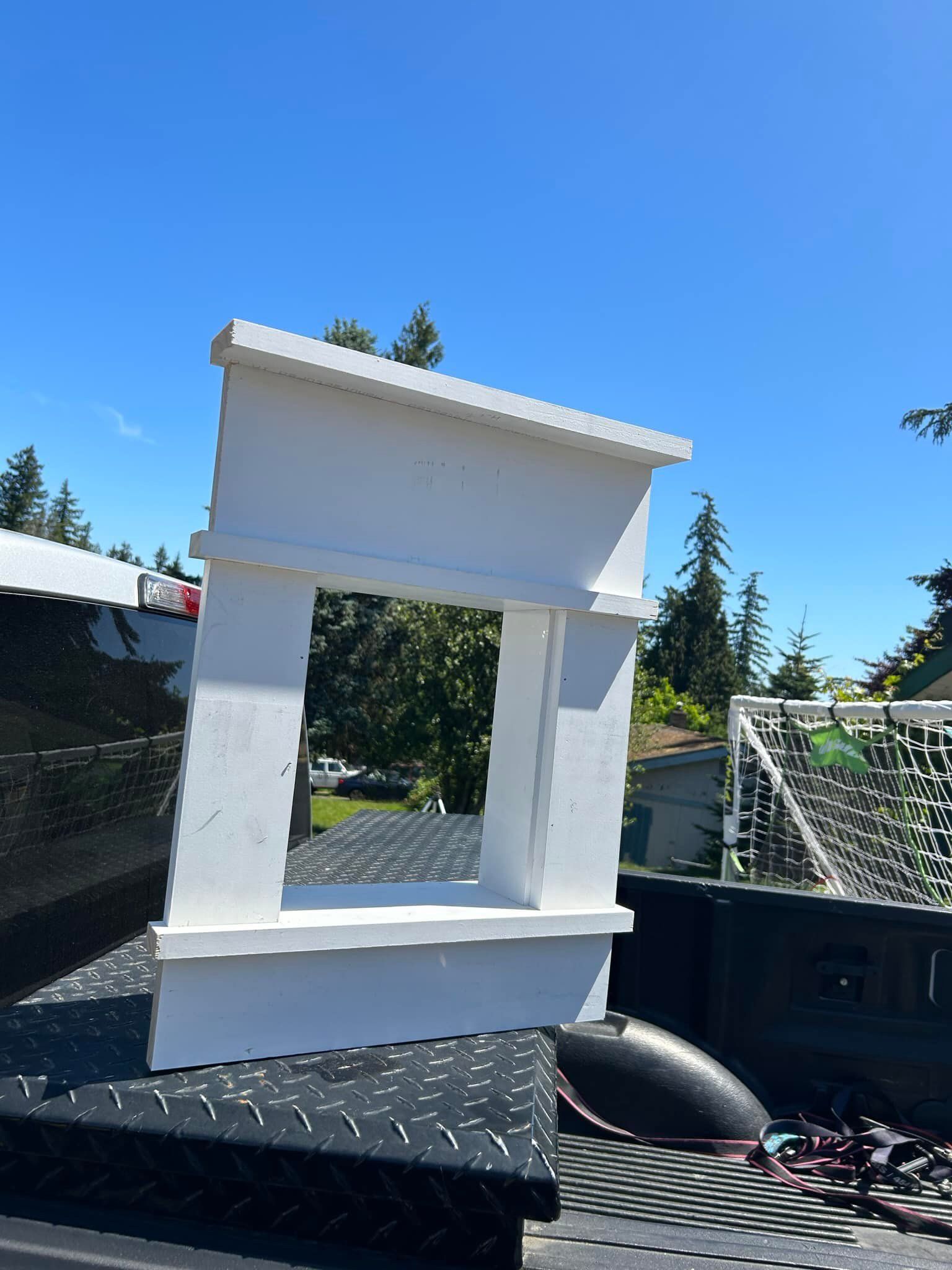 White decorative mantel or frame sitting on a black truck bed under a blue sky outdoors