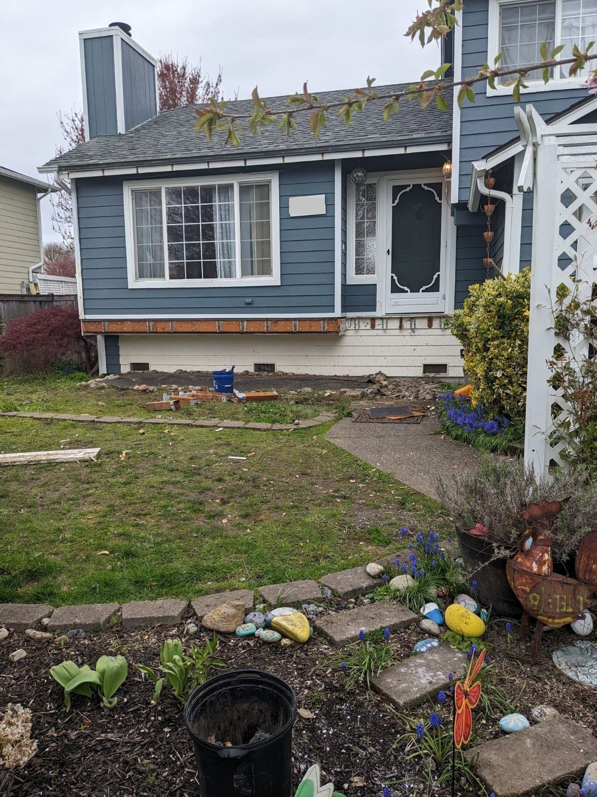 Small blue house with white trim, front yard path, and flower bed with garden decorations
