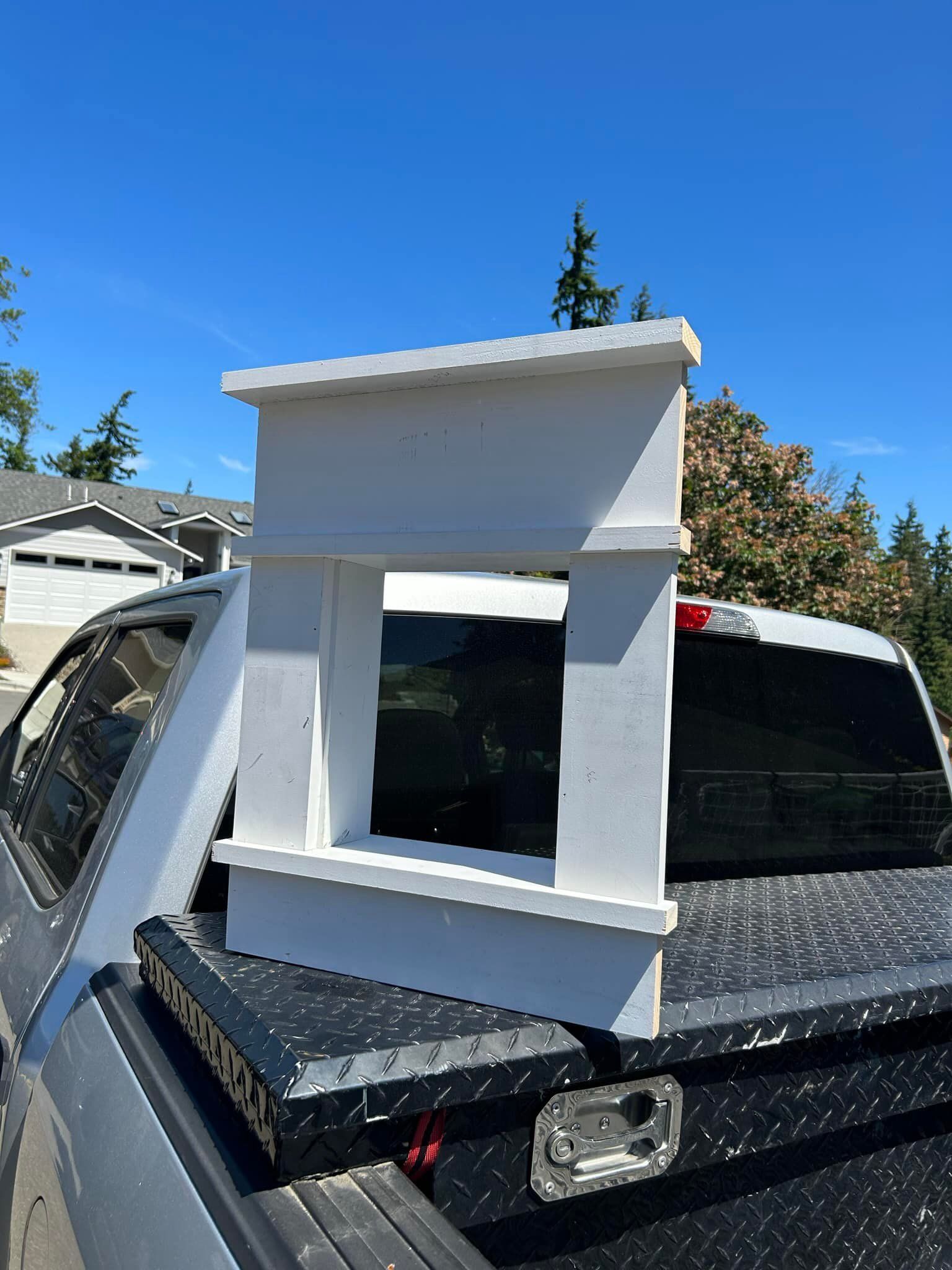 White box-like frame mounted on a silver pickup truck bed under a bright blue sky