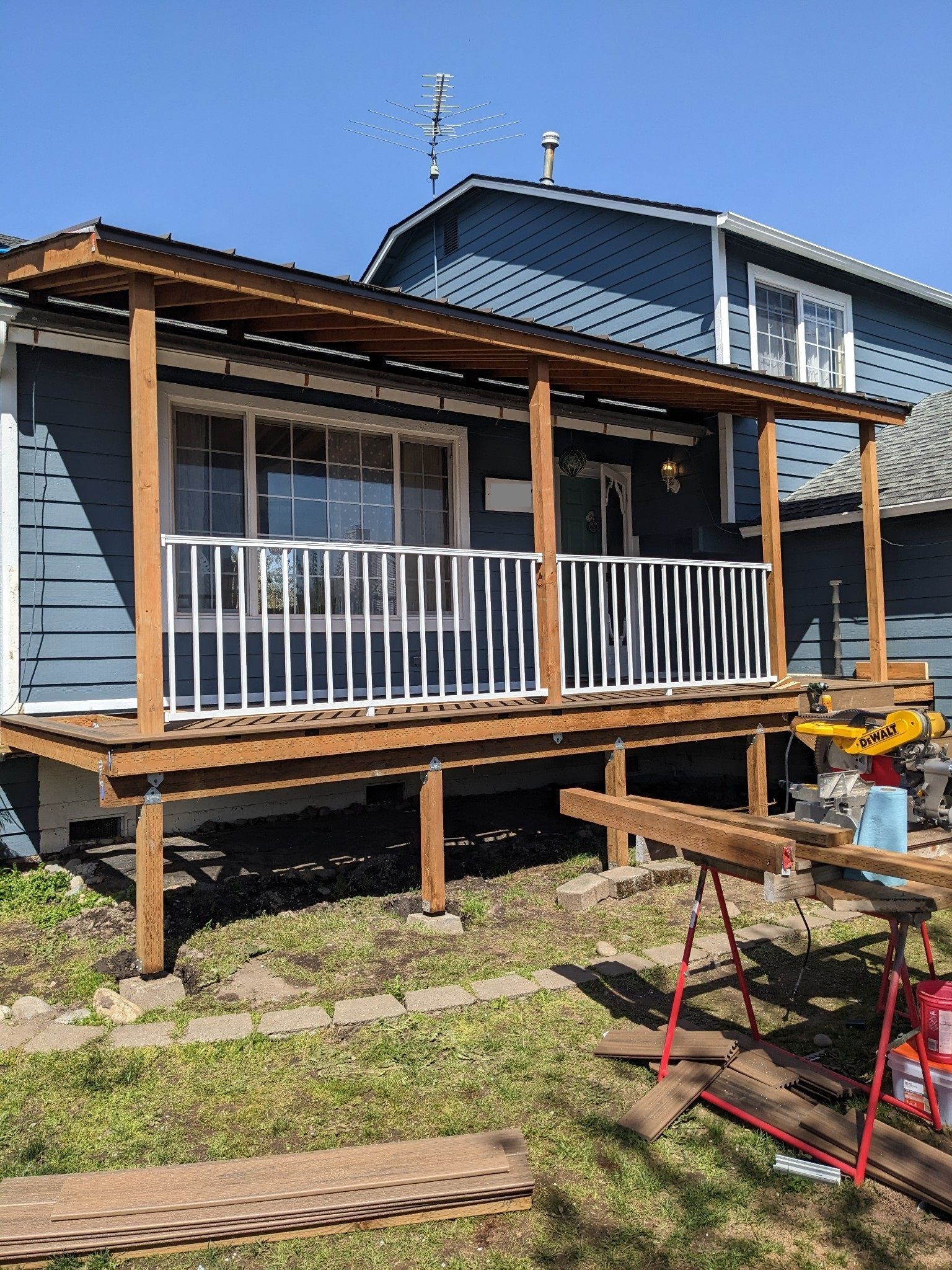 Blue house porch under construction with wooden posts, white railing, and tools in the yard
