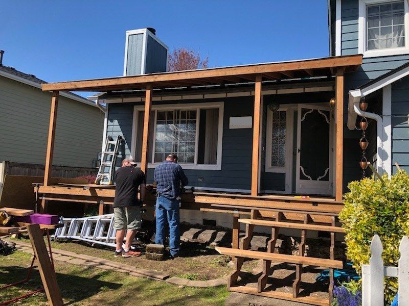 Two people working on a wooden porch deck under construction on a blue house