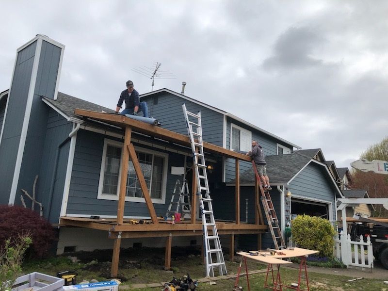 Workers repairing a blue house roof with ladders and wooden scaffolding under cloudy skies