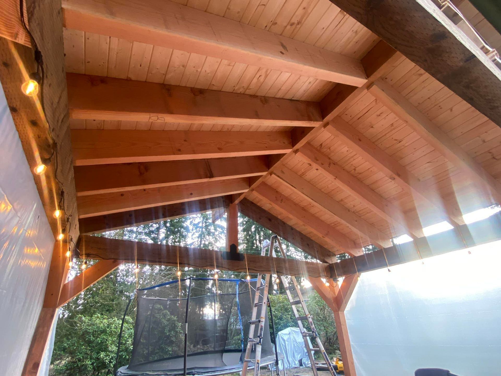 Wooden pavilion roof with exposed beams and string lights, overlooking a shaded outdoor deck and yard.